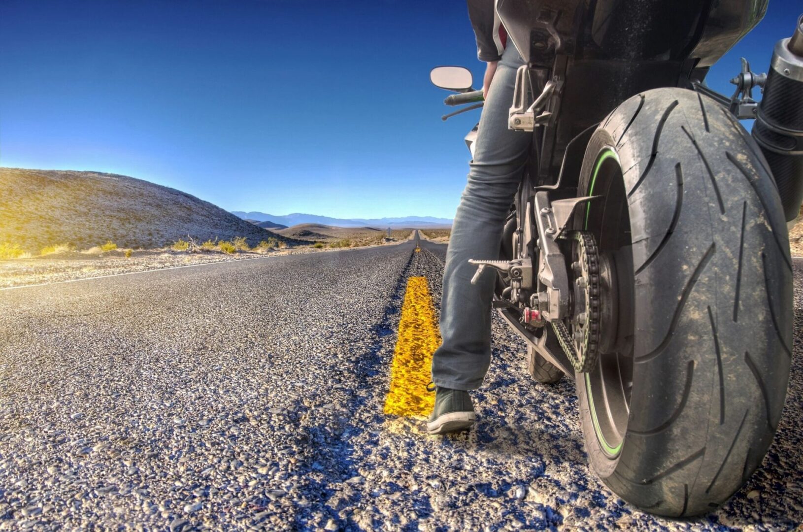 A person standing on the side of a road with their motorcycle.