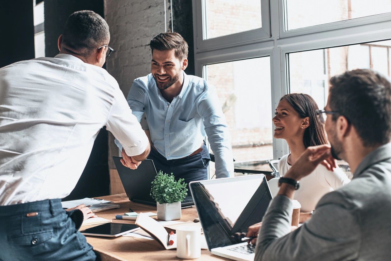 A group of people sitting around a table shaking hands.