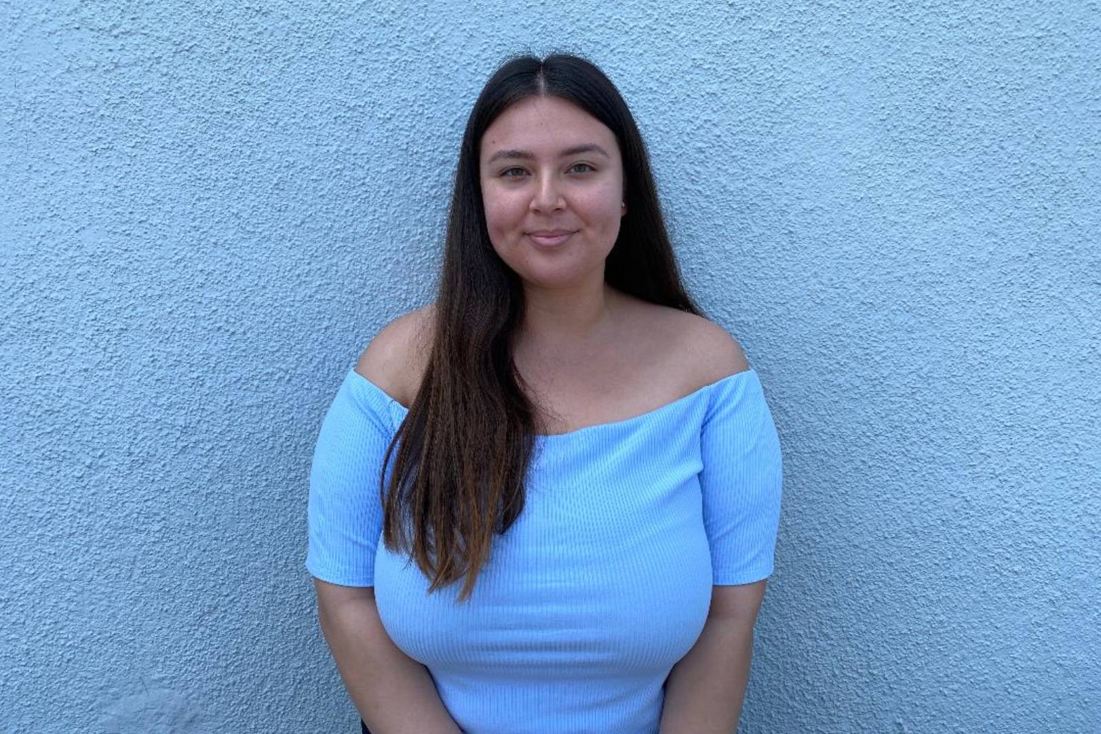 A woman in blue shirt standing next to wall.