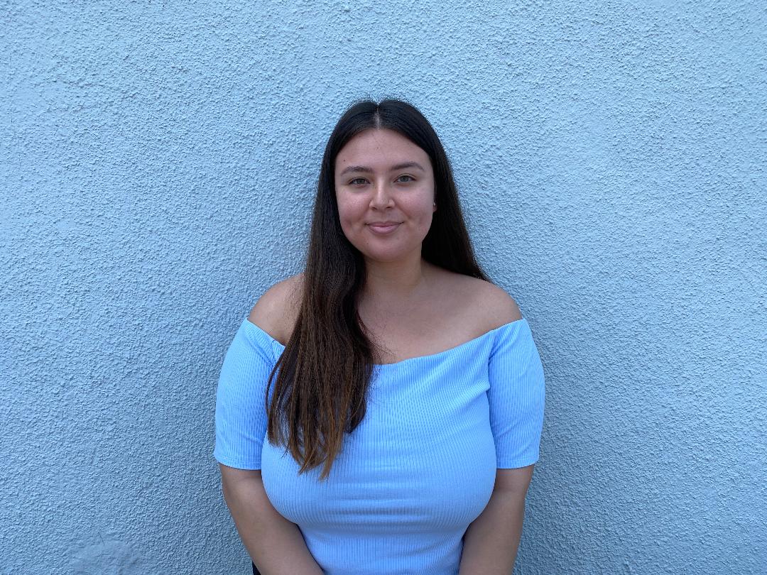 A woman in blue shirt standing next to wall.